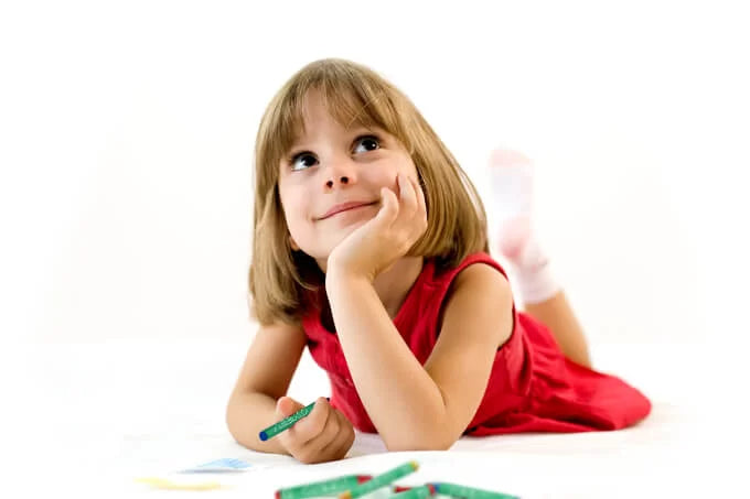 child staring dreamily with crayon in hand